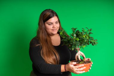 Küçük bir ağaç tutan genç bir kadın, yeşil arka plan herhangi bir renge dönüşebilir.