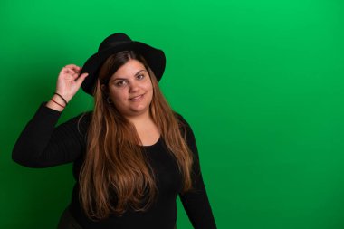 Siyah şapkalı genç bir kadın, el hareketleriyle yeşil arka planda herhangi bir renge dönüşebilir.