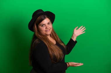 Siyah şapkalı genç bir kadın, el hareketleriyle yeşil arka planda herhangi bir renge dönüşebilir.