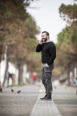 Doğal görünüşlü, dışarıda poz veren, günlük kıyafetler giyen, elinde akıllı bir telefon tutan ve konuşan, düzenleme yapmayan biri.