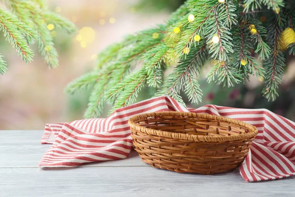 Empty basket with tablecloth on wooden table over pine tree branches background.  Winter mock up for design and product display.
