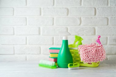 Spring cleaning concept with supplies on wooden table over white brick wall background