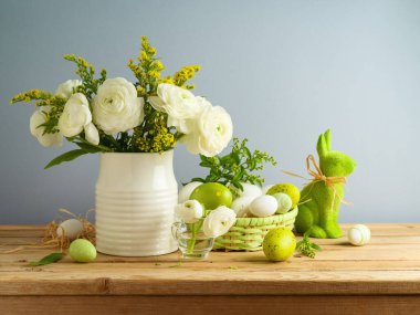 Paskalya tatili beyaz çiçekli buketli ve gri arkaplanlı ahşap masada Paskalya yumurtası süslemeli.