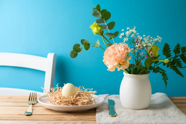 在蓝色背景的木制桌子上放有复活节彩蛋装饰的复活节花束和花盘 — 图库照片