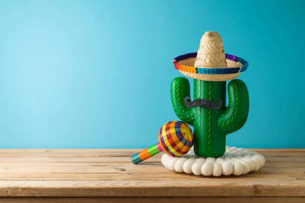 stock image Mexican holiday wooden table  with cactus,  party sombrero hat and maracas over blue background