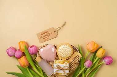 Anneler Günü 'nün kalp şeklinde hediye kutusu, özbakım ürünleri ve bej arka planda lale çiçekleri. Yukarıdan üst görünüm