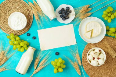 Yahudi bayramı Shavuot tebrik kartı peynir, süt şişesi ve ahşap masa arkasında buğday kulaklarıyla taklit edilir. Yukarıdan üst görünüm