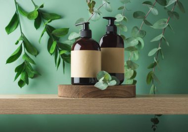 Doğal kozmetik ürünleri şişeleri. Banyodaki tahta kürsüde yeşil yapraklar üzerinde ambalaj tasarımı için etiketler var.