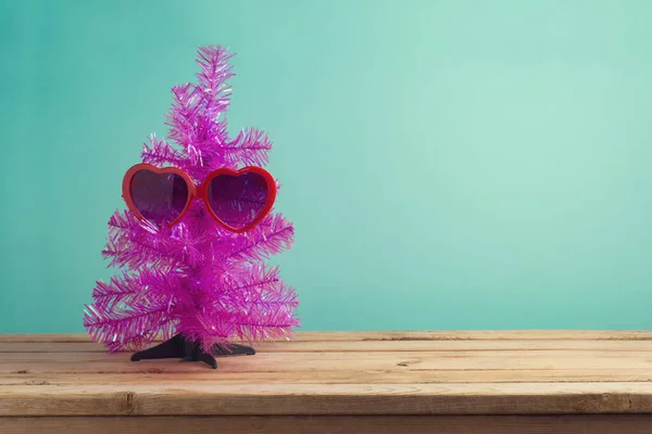 7月的圣诞节概念 蓝色薄荷背景下木制桌子上挂着有趣的粉色圣诞树和太阳镜 — 图库照片