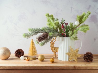 Vazoda çam ağacı dalları ve ahşap masada parlak arka planda altın süsler olan Noel süslemeleri.