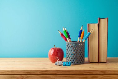 Kalemler, kitaplar ve elmalarla mavi arkaplan üzerindeki ahşap masaya geri dön.