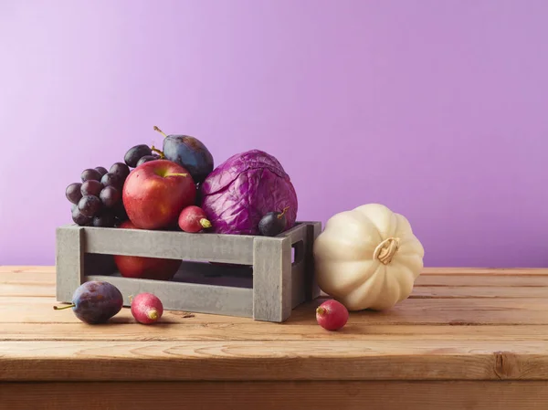 秋の収穫コンセプト 紫色の背景の上のテーブルの木箱のパンプキン リンゴ ブドウ — ストック写真
