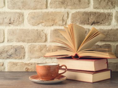Kahve fincanı ve kitaplar tuğla duvarın arkasında.