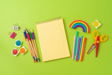 Okul konseptine dönersek, defter maketi ve modern yeşil arka planda okul malzemeleri. Üst manzara, düz uzanma