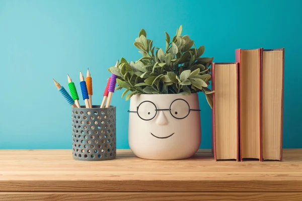 Back to school concept with books, pencils and cute funny plant on wooden table over blue background