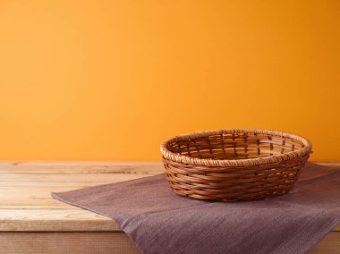 Boş sepet ve masa örtüsü, portakal rengi duvar arkaplanının üzerinde. Cadılar Bayramı ya da Şükran Günü tasarım ve ürün gösterisi için hazırlanır..