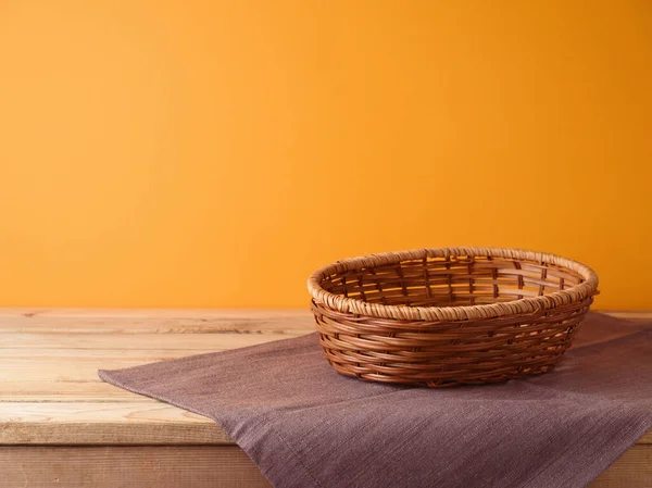 Empty basket with tablecloth on wooden table over orange wall background. Halloween or Thanksgiving  mock up for design and product display.