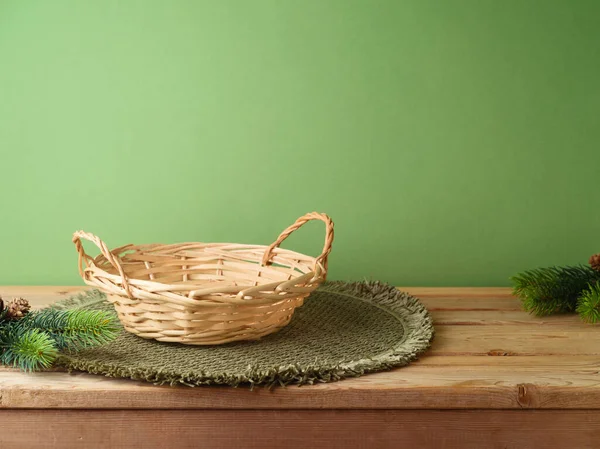Empty basket with place mat on wooden table over green wall and pine tree decoration background. Christmas mock up for design and product display.