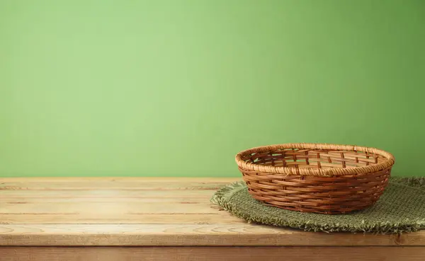 Empty basket with place mat on wooden table over green wall background. Kitchen mock up for design and product display.