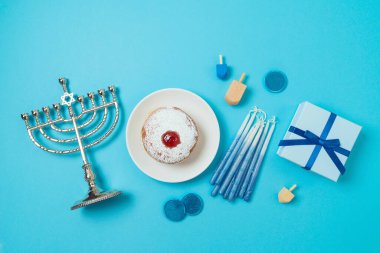 Yahudi bayramı Hanukkah üstten kompozisyonu menorah, geleneksel çörekler ve mavi arka planda hediye kutusu. Düz yatıyordu