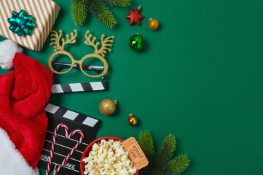 Noel gecesi ve patlamış mısır, Noel Baba şapkası, dekorasyon ve yeşil arka planda film alkışlama tahtası ile parti konsepti. Üst manzara, düz uzanma