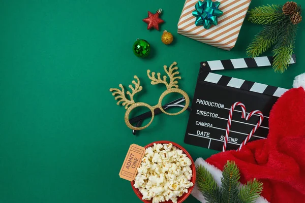 Christmas movie night and party concept with  popcorn, Santa hat, decorations and movie clapper board on green background. Top view, flat lay