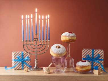 Yahudi bayramı Hanuka yaratıcı kompozisyonu menorah, geleneksel çörekler ve ahşap masa üzerinde modern arka plan üzerinde hediye kutusu