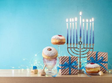 Yahudi bayramı Hanuka yaratıcı kompozisyonu menorah, geleneksel çörekler ve ahşap masa üzerinde mavi arka plan