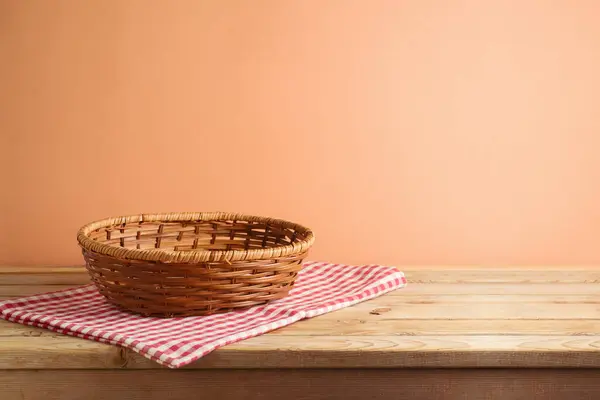 Empty basket on  table with red checked tablecloth over peach color background.  Kitchen or bakery mock up for design and product display