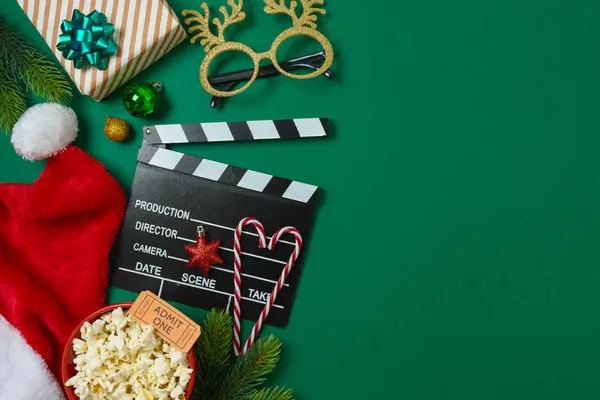 Christmas movie night and party concept with  popcorn, Santa hat, decorations and movie clapper board on green background. Top view, flat lay