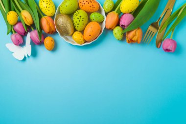 Paskalya bayramı sofrasında mavi arka planda paskalya yumurtaları ve lale çiçekleri. Üst manzara, düz uzanma