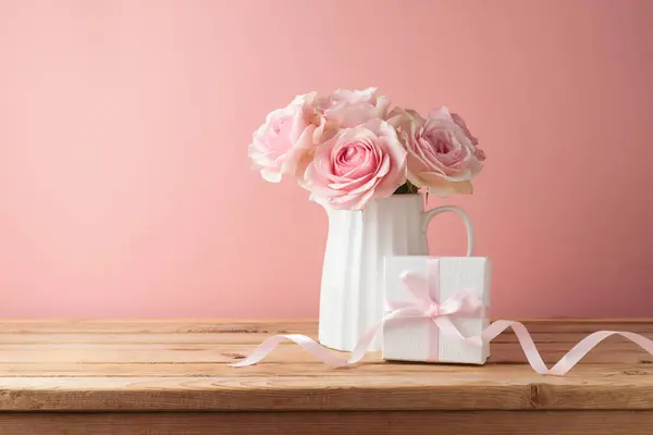 Romantic rose flower bouquet with gift box on wooden table over pink background