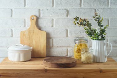 Mutfak masasının üzerinde boş ahşap bir podyum var. Arkaplanda da yemek kavanozları ve bitkiler var. Mutfak tasarım ve ürün gösterimi için hazırlandı.