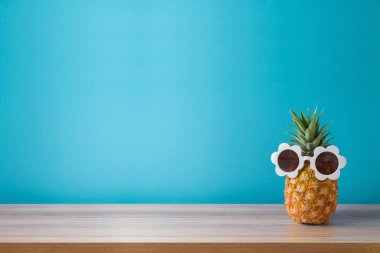 Mavi arkaplan üzerinde güneş gözlüklü ananas ve ürün sergisi için boş alan. Yaz tatili kavramı