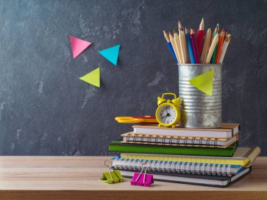 Kalemler, defterler ve alarm saatiyle tahta masanın üzerine, tahta arka planda okula geri dön.