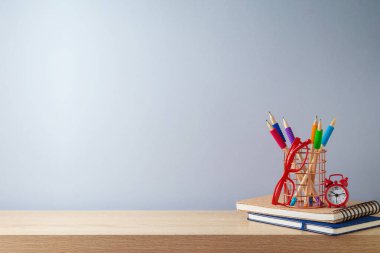 Okul arkaplanına tahta masa, kalemler, defter, çalar saat, gözlük ve ürün gösterimi için boş alan ile geri dön