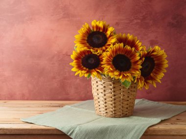 Sonbahar arkaplanı, hasır sepetin içindeki ayçiçekleri ahşap masanın üzerinde. 