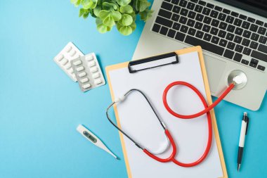 Mavi arka planda dizüstü bilgisayar, not defteri ve doktor steteskopu ile çevrimiçi doktor danışmanlığı kavramı. Üst manzara, düz uzanma