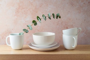 Mutfak beyaz bulaşık takımı, kahve fincanları ve tabaklar ahşap rafta, arka planda taş var.