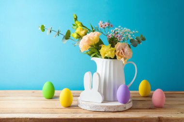 Paskalya tatili yumurta süslemesi ve çiçek buketi ahşap masa üzerinde mavi arka plan üzerinde
