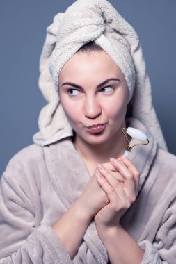 Women's beauty and spa. Beautiful woman using guasha jade stone roller massaging her face for a radiant complexion and healthy skin