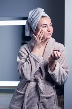 Girl in a towel on her head in a cosmetic mask on a gray background