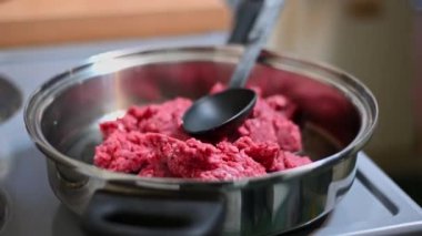 A juicy raw minced beef sizzles in a hot pan as a black plastic spoon rests on top, ready for food preparation.