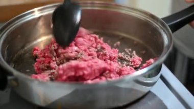 Large black plastic spoon stirs raw minced beef as it begins to brown in a hot pan