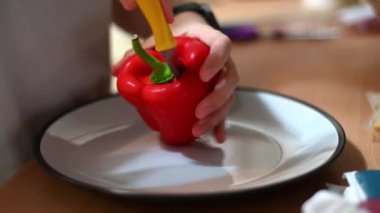 Woman's hands use a sharp knife to cut and remove the centre of a red pepper