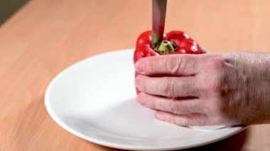 Kırmızı bir çan biberi, beyaz bir tabakta keskin bir bıçakla tohumları ve içindeki eti çıkararak pişirmeye hazırlanıyor..