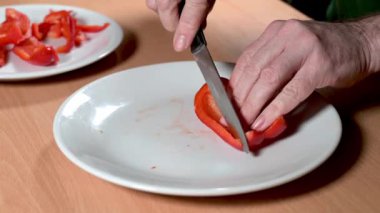 Bir adamın elleri keskin bir bıçakla canlı kırmızı biberi beyaz bir tabakta dikkatlice dilimliyor..