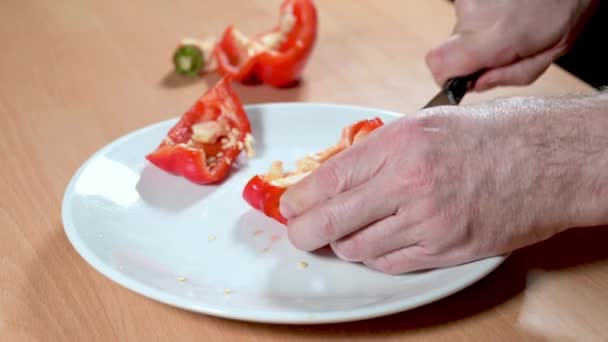 一个人的手用一把锋利的小刀巧妙地从盘子里的红椒中取出种子和白肉 — 图库视频影像
