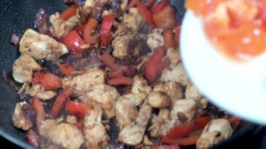 Doğranmış domateslerin sıcak tavaya tavuk kübü, kırmızı biber ve kızarmış kırmızı soğanla yavaşça eklenmesi..