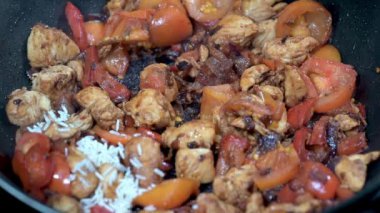 Pirincin taze tavuk, olgun domates ve kızarmış soğanla dolu sıcak bir tavaya eklenişini izleyin..